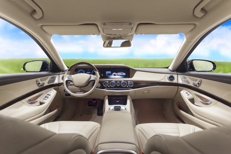 Emisiones reducidas en el interior Interior de color beige de un coche de clase superior que se ve a través del parabrisas sobre una pradera verde y cielo azul