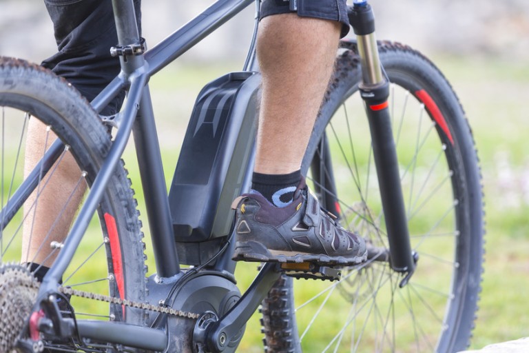 Bicicleta electrónica Piernas y zapatillas en los pedales de una bicicleta electrónica negra