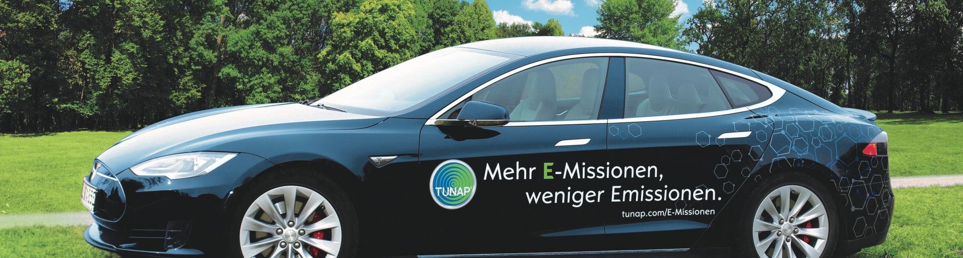 Side view of a dark blue sports car with white lettering and a TUNAP logo on a green meadow
